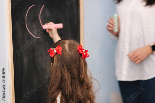 Children write letters on blackboard. Teacher teaches kids. Prescool photo