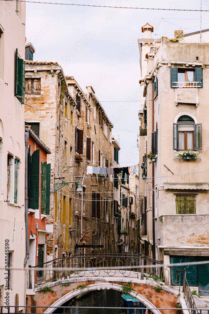 Close-ups of building facades in Venice, Italy. A narrow Venetian canal, between two houses drying clothes on a rope. A small stone bridge with metal railings