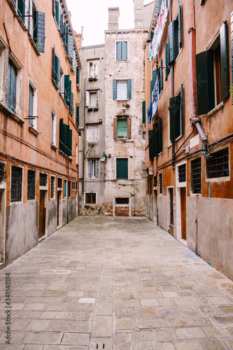 Close-ups of building facades in Venice, Italy. Dead end Venetian street. Five-story houses with blue-green wooden shutters on the windows, linen is dried in the windows, an old stone floor.