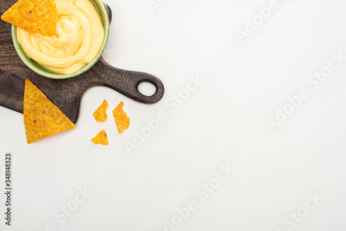 top view of corn nachos with cheese sauce on wooden cutting board on white background photo