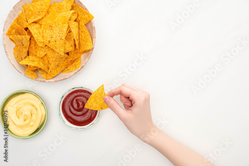 cropped view of woman eating corn nachos with cheese sauce and ketchup on white background photo