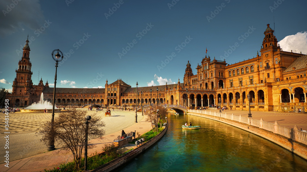 Seville, Spain - February 18th, 2020 - the Plaza de Espana / Spain Square with the canal, wood rowing boats and tourists visiting, in Seville City, Spain.