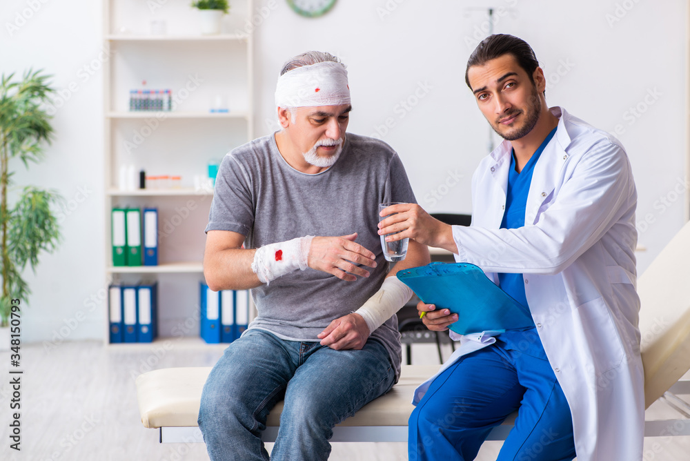 Fototapeta premium Young male doctor and old patient in first aid concept