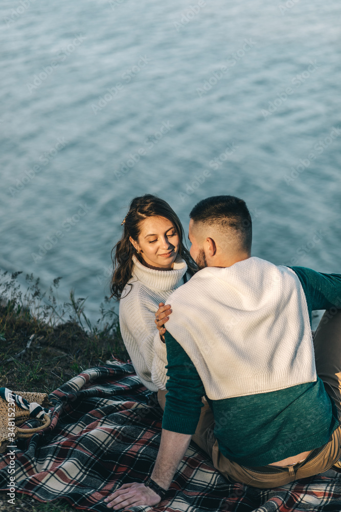 A guy and a girl love each other, smile, hug, kiss, laugh, enjoy life in the forest on a cliff, in the grass. Girl holding a film camera in her hands, photographs a guy, sunset in the background.
