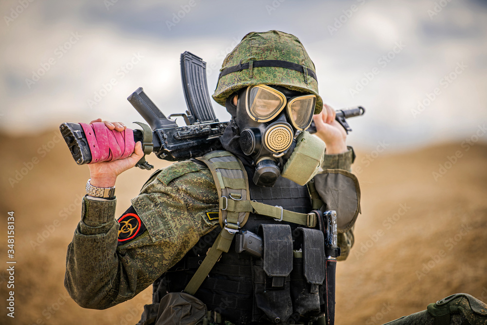 Fototapeta premium military man in a gas mask with a weapon stands in the middle of the desert
