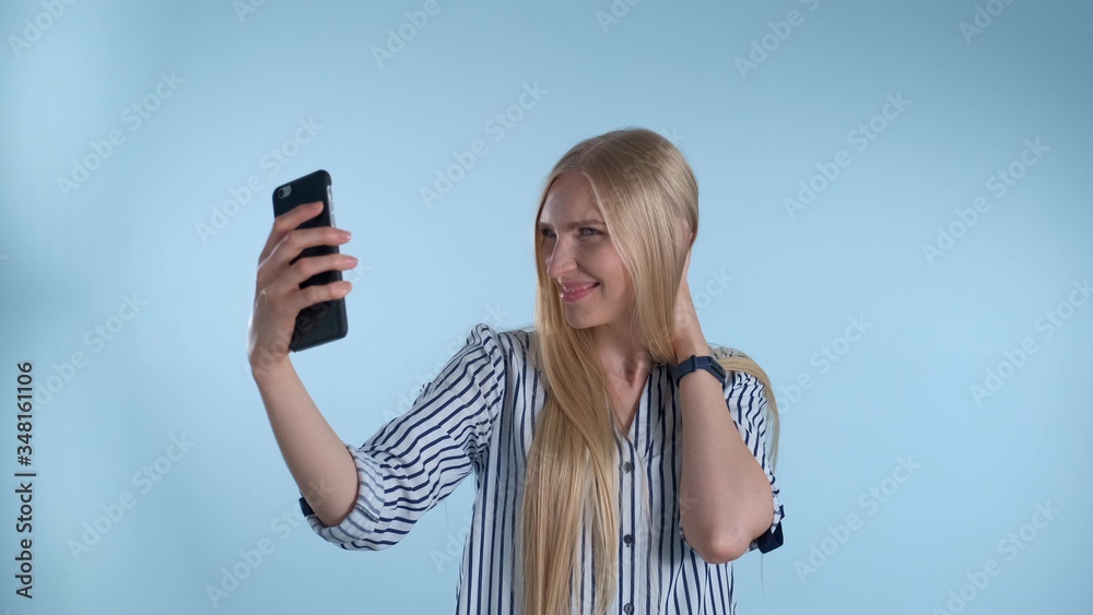 Attractive blonde lady making selfie on smartphone on blue background. She posing and smiling to the camera. Attractive blonde lady making selfie on smartphone on blue background. She posing and smiling to the camera.