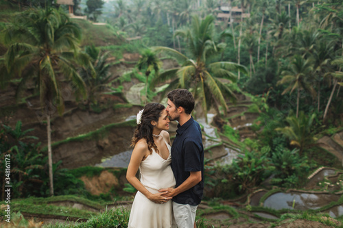 Young latin pregnant woman with husband with amazing view of Ubud rice terraces. Pregnant couple happy together.