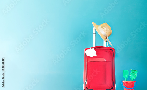 Red suitcase with straw hat, Coronavirus mask on green background and children's bucket