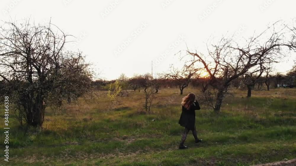 Aerial view of a young girl who is walking in the spring garden in the rays of the setting sun and is dancing merrily Aerial view of a young girl who is walking in the spring garden in the rays of the setting sun and is dancing merrily