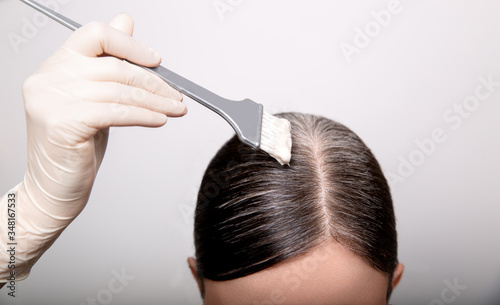 Foto Woman dyeing grey hair root with brush and hair color, close up