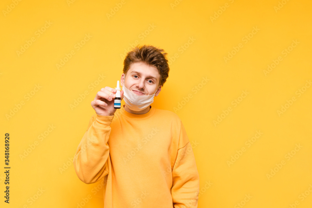 A funny guy with a removed mask stands on a yellow background, looks at the camera with a smile on his face and shows nasal spray to the camera. Fighting the undead in a pandemic. COVID-19. Quarantine A funny guy with a removed mask stands on a yellow background, looks at the camera with a smile on his face and shows nasal spray to the camera. Fighting the undead in a pandemic. COVID-19. Quarantine