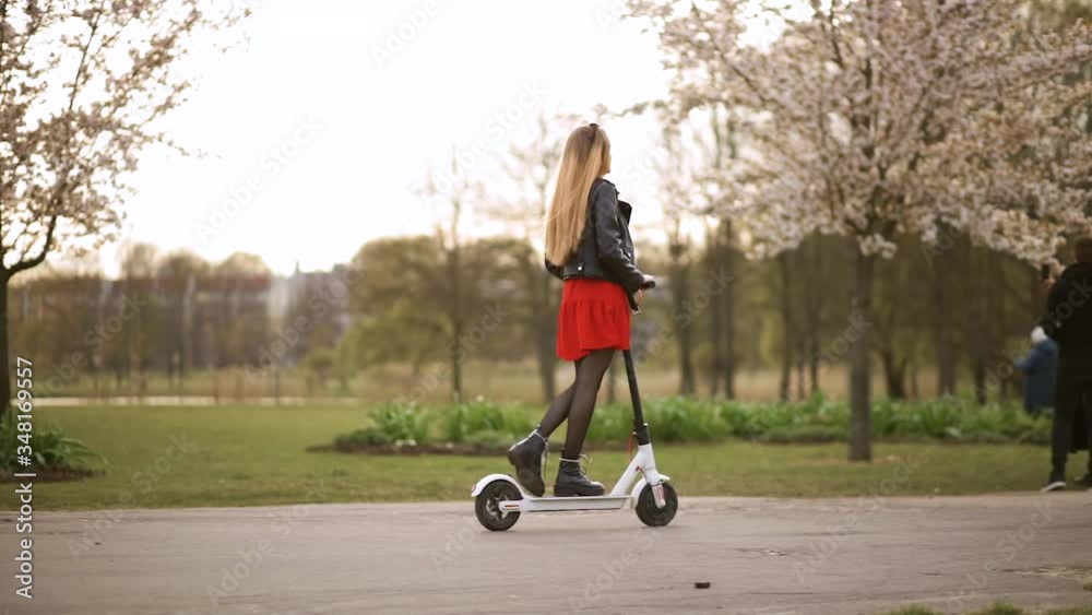 Young stylish woman rides electric scooter in city park