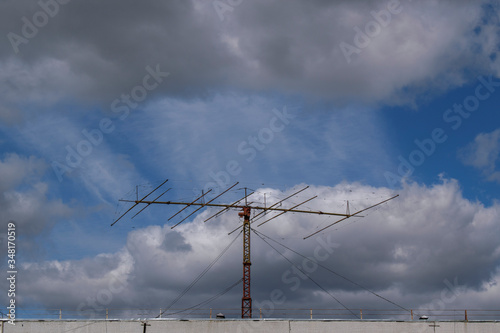 Amateur radio antenna on roof of building. Transceiver directional action. Metal construction with supporting cables. Sky with clouds. photo