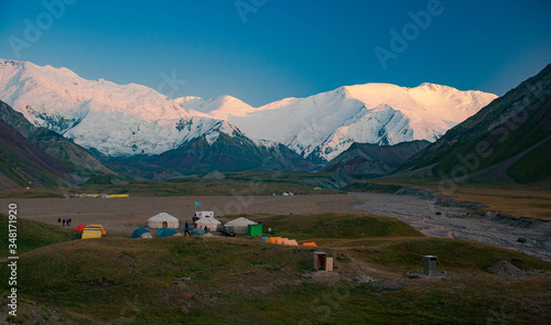 Scenic summer landscape of snowy mountainpeaks. Tent camp with yurts in the valley. Sunset.