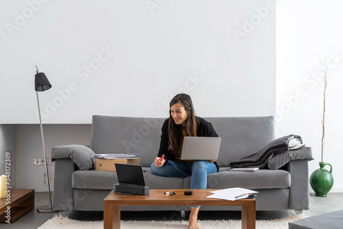Young woman with laptop and tablet telecommuting on the sofa at her home