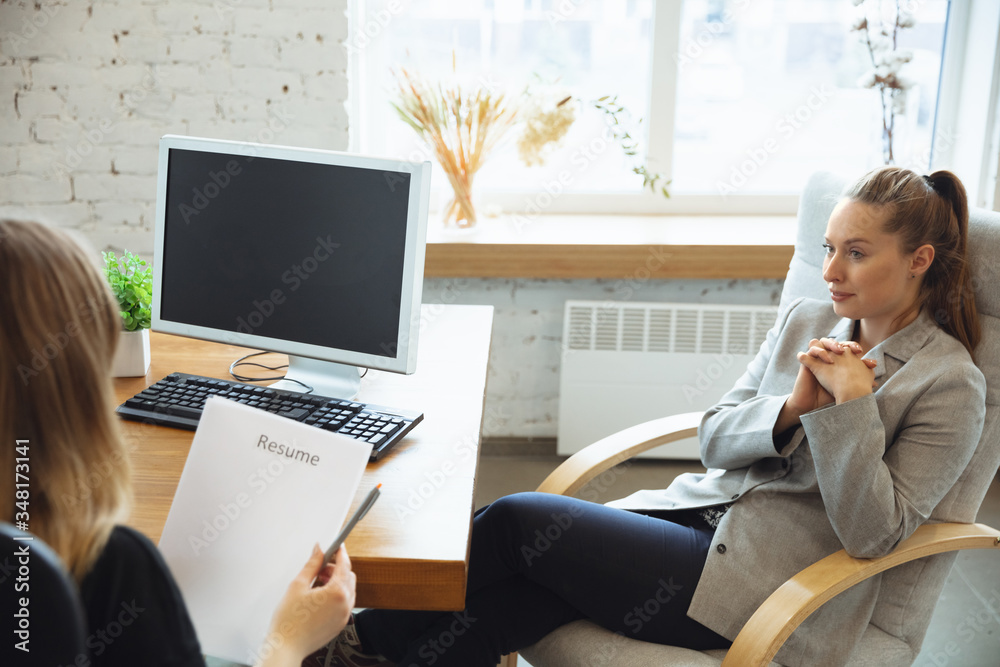 Obraz premium Young woman sitting in office during the job interview with female employee, boss or HR-manager, talking, thinking, looks confident. Concept of work, getting job, business, finance, communication.