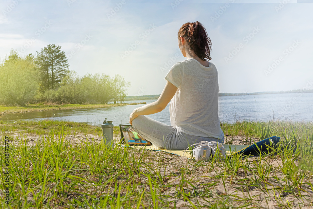 A female stretches out on a yellow rug on the riverbank with a tablet, outdoor. The concept of online tutorials, distance learning. A female stretches out on a yellow rug on the riverbank with a tablet, outdoor. The concept of online tutorials, distance learning.