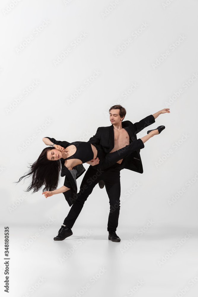 Obraz premium Young and graceful ballet dancers in minimal black style isolated on white studio background. Art, motion, action, flexibility, inspiration concept. Flexible caucasian ballet dancers, weightless jumps