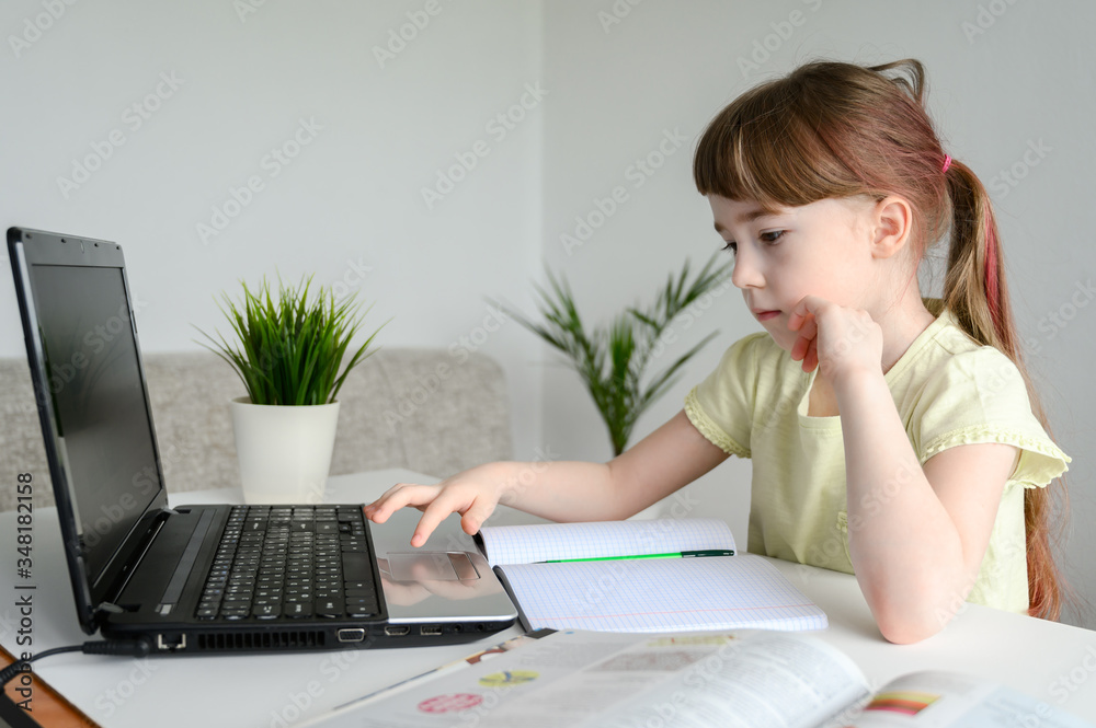 Distance learning online education. Schoolgirl studying at home, using laptop. Caucasian kid sits by the table and doing school homework. Copy space, horizontal orientation.