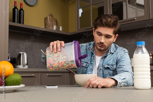 Selective focus of man pouring cereals in bowl near bottle of milk and fruits on kitchen table