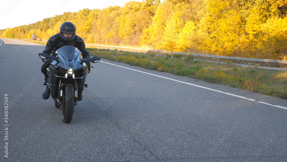 Young man in helmet riding fast on modern sport motorbike at autumnal highway. Motorcyclist racing his motorcycle on country road with headlights on. Guy driving bike during trip. Concept of freedom Young man in helmet riding fast on modern sport motorbike at autumnal highway. Motorcyclist racing his motorcycle on country road with headlights on. Guy driving bike during trip. Concept of freedom