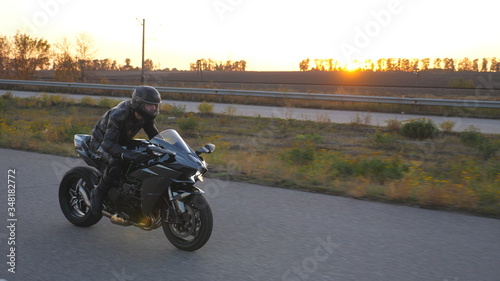 Motorcyclist races his motorcycle on autumnal country road. Man in helmet rides fast on modern sport motorbike at highway with sun flare at background. Guy driving bike during trip. Concept of freedom