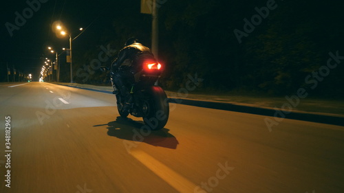 Man riding fast on modern sport motorbike at nighty city street. Motorcyclist racing his motorcycle on empty road. Guy driving bike at dusk. Concept of freedom and adventure. Low angle of view Closeup © olehslepchenko