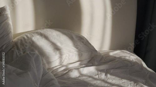 Bedroom with unmade bed in the morning, sunlight falling on bed, curtains moved by the wind. photo