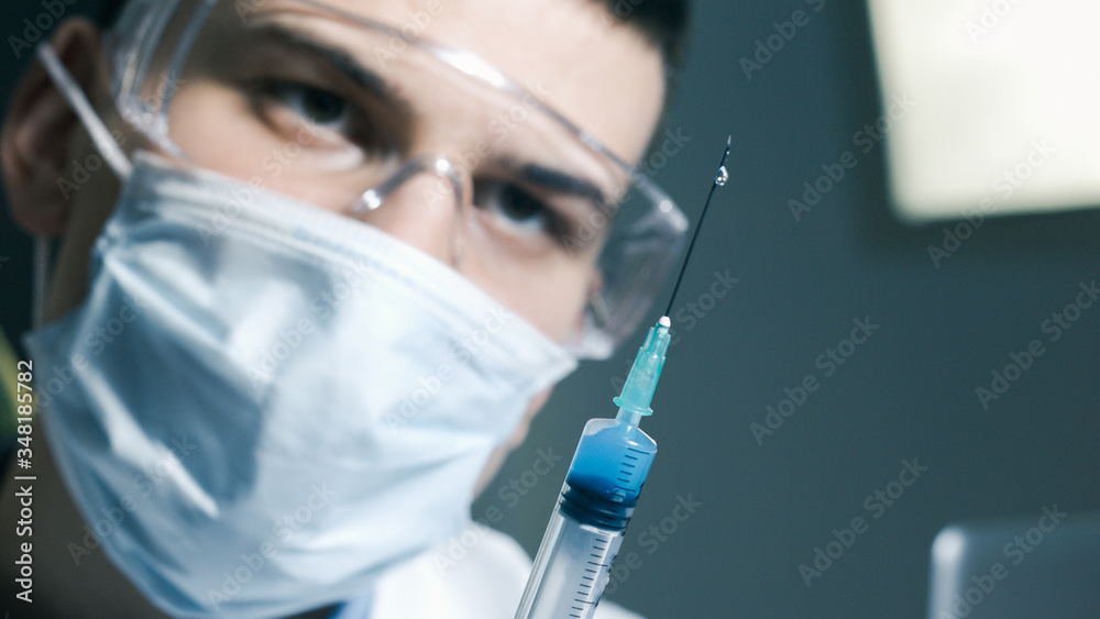 Doctor with syringe is preparing for vaccine injection and looking at needle, close-up. Doctor with syringe is preparing for vaccine injection and looking at needle, close-up.