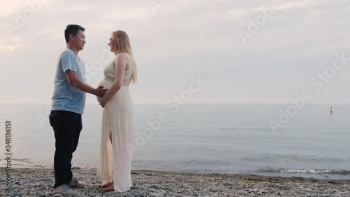 A young multi-ethnic couple stands on the seashore, a pregnant woman and an Asian man photo