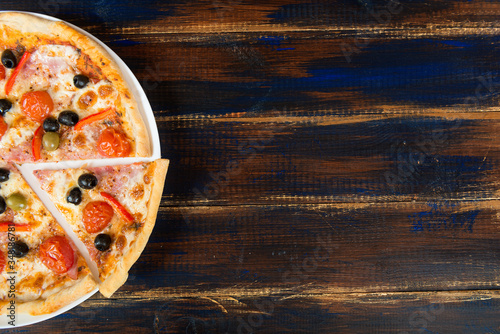 Fresh pizza with tomato sauce, black olives, mozzarella cheese, ham on wooden table closeup