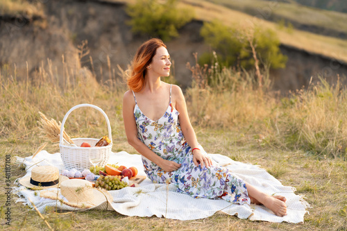Beautiful red-haired girl enjoys the sunset on the nature. Picnic in the field.