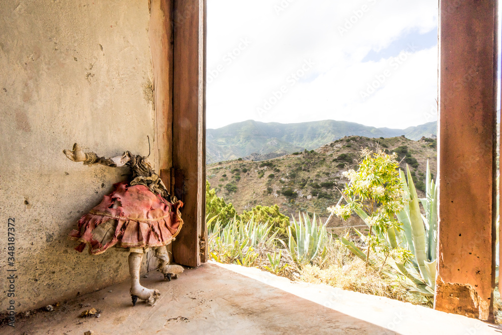 Obraz premium dirty faceless doll standing in an abandoned house in the mountains of La Gomera, Canary islands. Cursed, broken and evil girl mannequin in a red worn and damaged dress. Scary, haunted and lost place