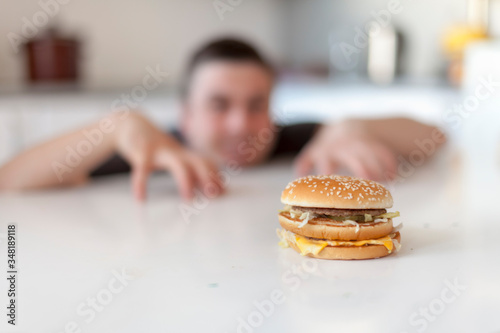 The man looks with cunning eyes at a cheeseburger lying on the table. Burger is not healthy food. Very hungry guy. Diet concept.