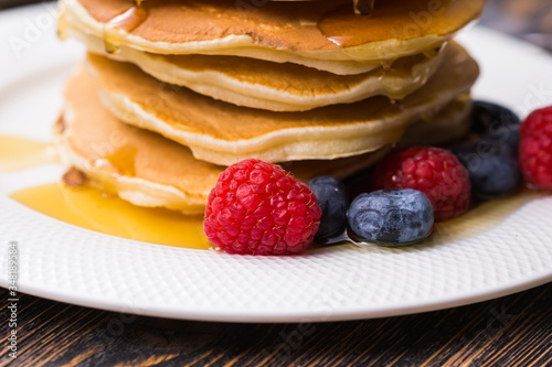 Pile of pancakes with blueberries and raspberries and maple syrup for breakfast on wooden table.