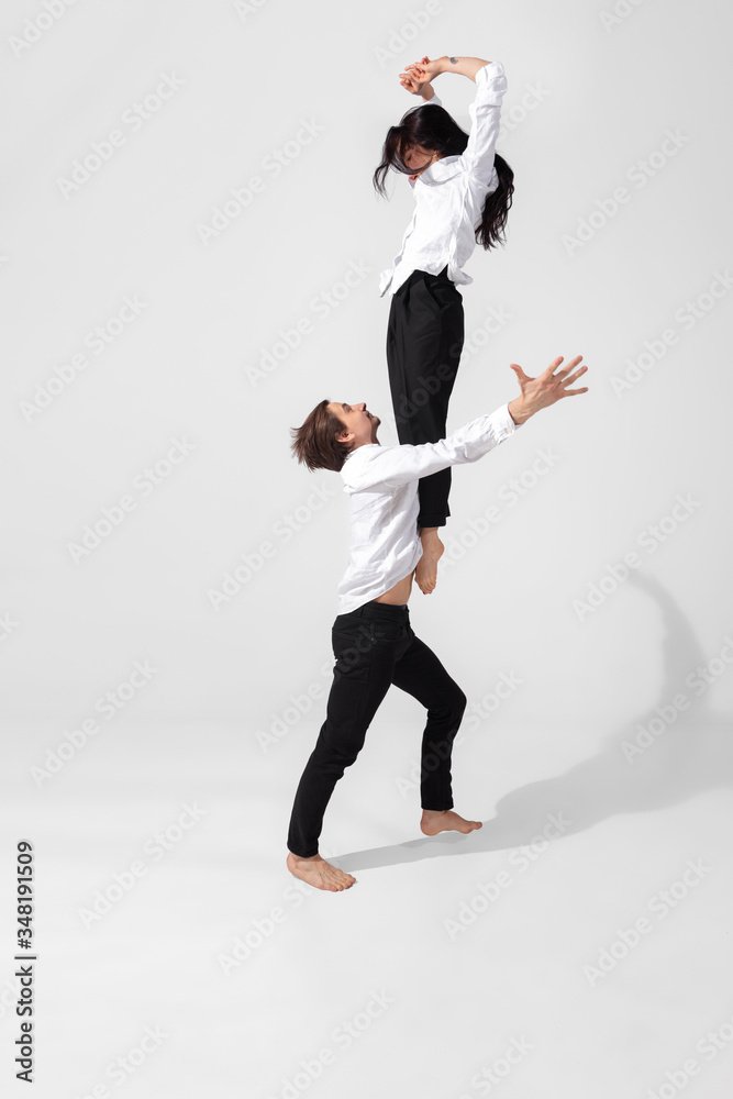 Young and graceful ballet dancers in minimal black style isolated on white studio background. Art, motion, action, flexibility, inspiration concept. Flexible caucasian ballet dancers, weightless jumps