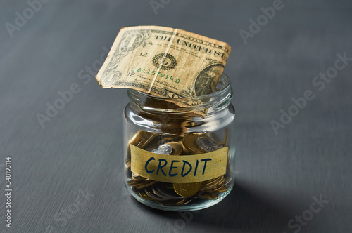 Glass jar with coins and inscription credit, banknote of one dollar on concrete desk