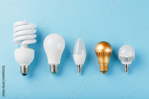 One Golden light bulb in a row of energy-saving white lamps on a blue background.