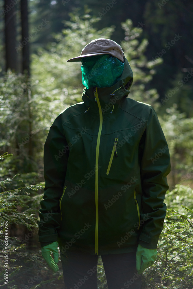 Unrecognizable man in a green plastic mask in the forest as a symbol.