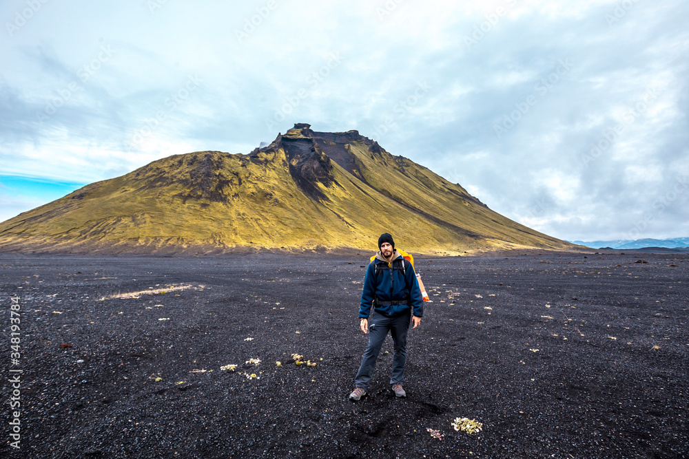 A young man in volcanic ash and a green mountain in the background on the 54 km trek from Landmannalaugar, Iceland