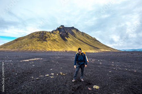 A young man in volcanic ash and a green mountain in the background on the 54 km trek from Landmannalaugar, Iceland