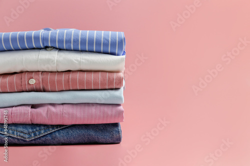 Cropped image with stack of colorful perfectly folded clothing items. Macro shot of pile of different pastel color shirts, sweaters & pants. Close up, copy space, background. photo