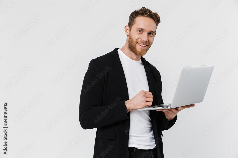 Image of handsome pleased man in jacket smiling and using laptop Image of handsome pleased man in jacket smiling and using laptop