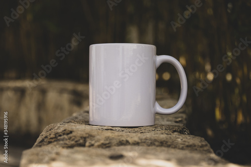 White Coffe mug with no design outside over the rocks with the blured background, perfect for business. Can be used for muck-ups and used your design