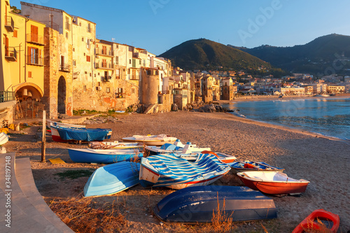 Boats on the beach and sunny houses in coastal city Cefalu at sunset, Sicily, Italy