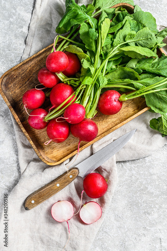 Fresh radishes with tops in a wooden bowl. Farm organic vegetables. Gray background. Top view