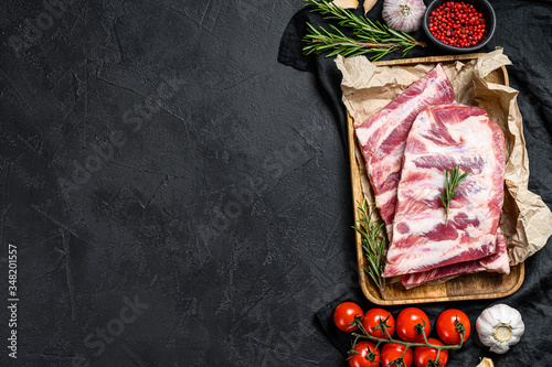 Fresh raw pork ribs with rosemary and garlic in a wooden bowl. Black background. Top view. Space for text