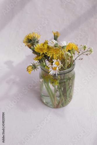 dandelions and daisies in a jar on a white background