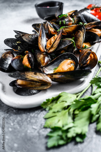 Raw mussels in shells on a chopping Board. The concept of cooking seafood in tomato sauce with parsley. Gray background. Top view