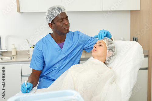 Male examining patient face skin before aesthetic procedure  writing to workbook